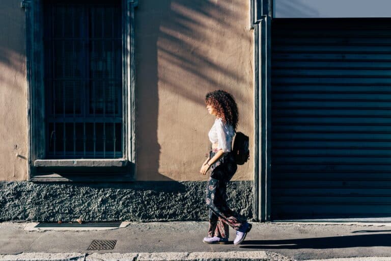 Woman passing roller shutters of closed shop, Milan, Italy